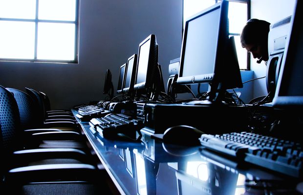 A row of desk screens and keyboards in a dim room, one person working at the far end