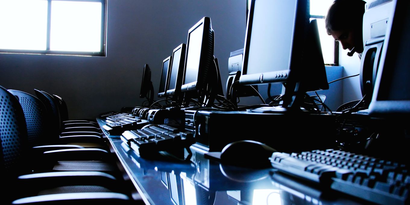 A row of desk screens and keyboards in a dim room, one person working at the far end