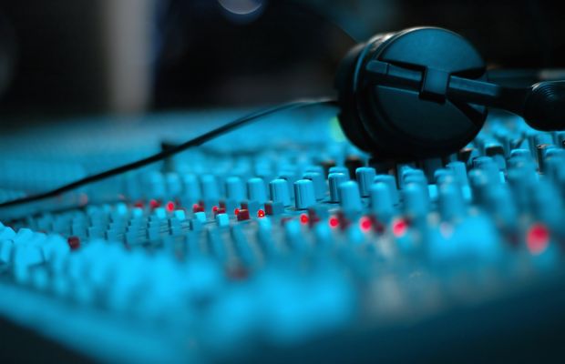 Headphones resting on the faders of a sound mixing desk lit in blue