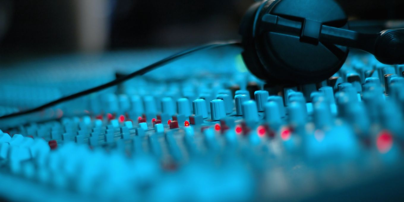 Headphones resting on the faders of a sound mixing desk lit in blue