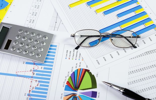Printed bar charts and tables with reading glasses, a calculator and a pen