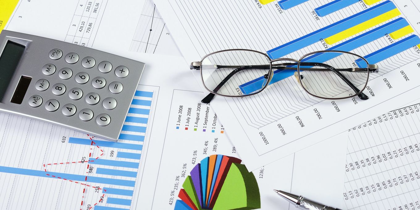 Printed bar charts and tables with reading glasses, a calculator and a pen